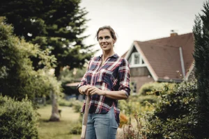 A proud homeowner standing outside the front of her home with gardening tools.